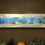 Wide wall-mounted aquarium with colorful decorations.