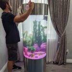 Man cleaning large cylindrical fish tank.