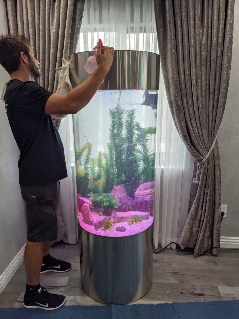 Man cleaning large cylindrical fish tank.